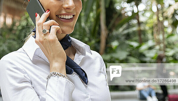 Lächelnde weibliche Flugbegleiterin  die im Garten mit ihrem Smartphone telefoniert