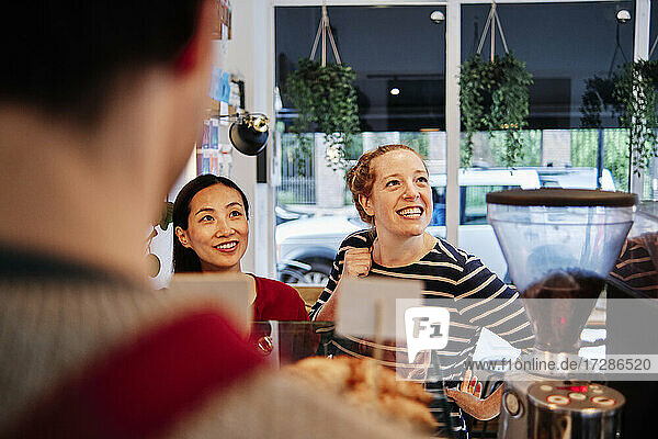 Lächelnde Freundinnen schauen weg  während sie vor dem Besitzer eines Cafés stehen