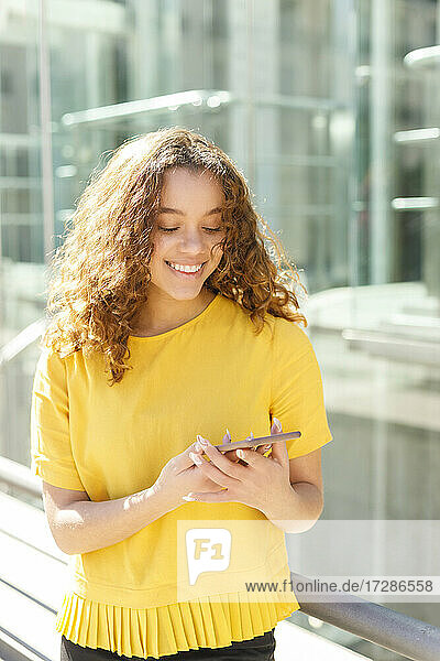 Lächelnde junge Frau  die an einem sonnigen Tag ein Mobiltelefon benutzt
