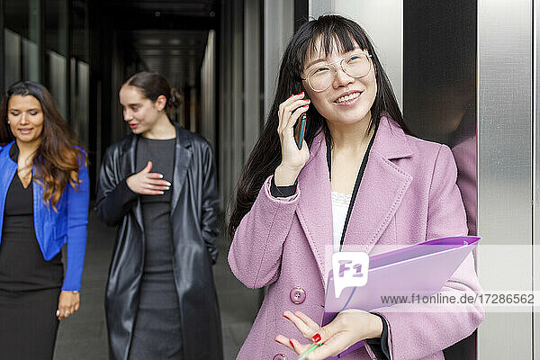 Weibliche Unternehmerin im Gespräch am Handy mit Kollegen im Hintergrund