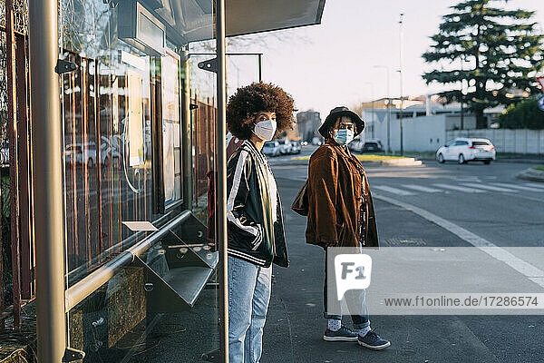 Junge Freundinnen mit Gesichtsmaske warten am Busbahnhof