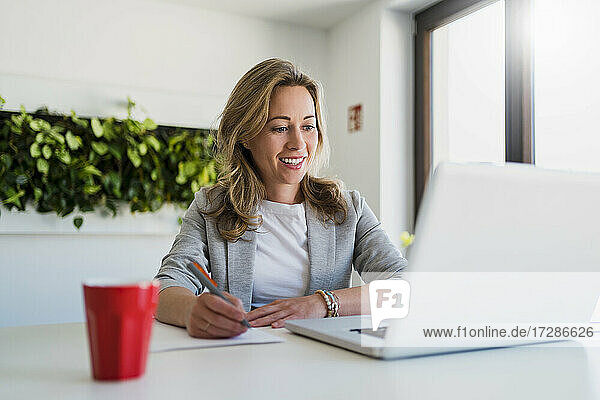 Lächelnde Geschäftsfrau mit Blick auf den Laptop im Büro