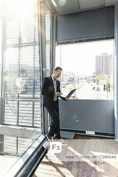 Businessman with laptop leaning on window at office
