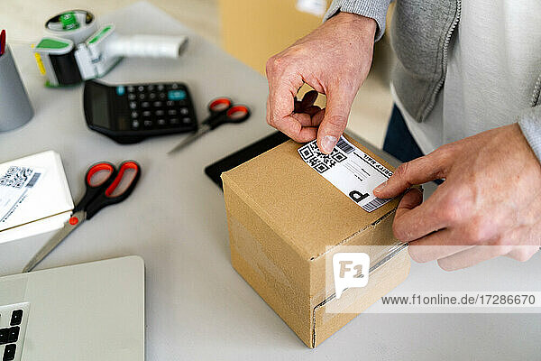 Männlicher Unternehmer  der einen QR-Code auf ein Kartonpaket am Schreibtisch klebt