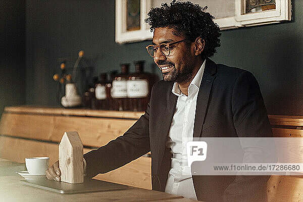 Lächelnder reifer Geschäftsmann  der ein Hausmodell betrachtet  während er im Cafe sitzt