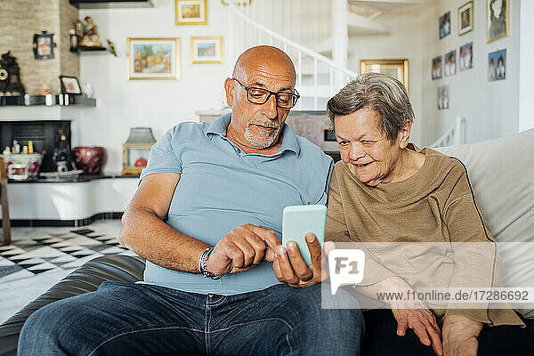 Senior man using smart phone while sitting by mother on sofa in living room