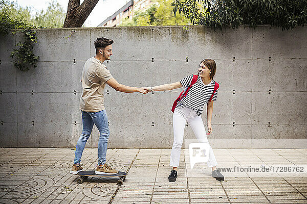 Boyfriend holding hand of girlfriend while skateboarding on footpath