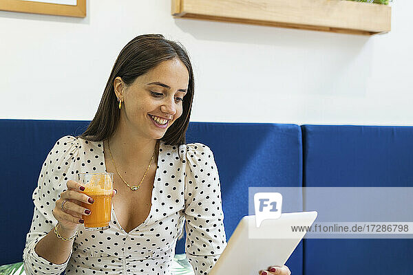 Lächelnde junge Frau  die in einem Restaurant einen Saft trinkt und ein digitales Tablet benutzt