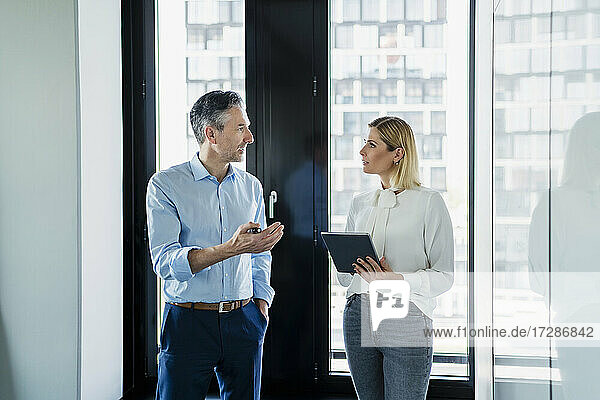 Geschäftsfrau  die ein digitales Tablet hält und einen männlichen Kollegen betrachtet  der eine Strategie im Büro diskutiert