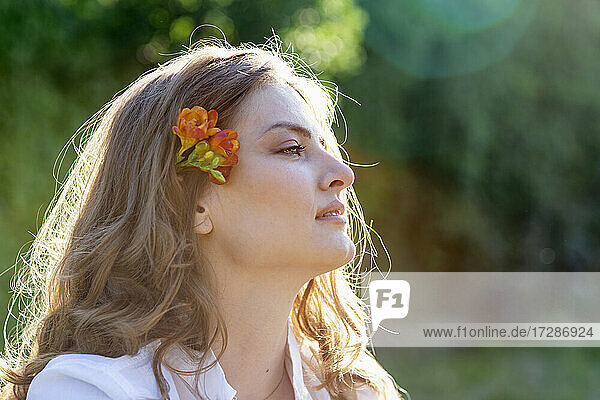 Schöne junge Frau mit blondem Haar trägt Freesienblüten und schaut weg