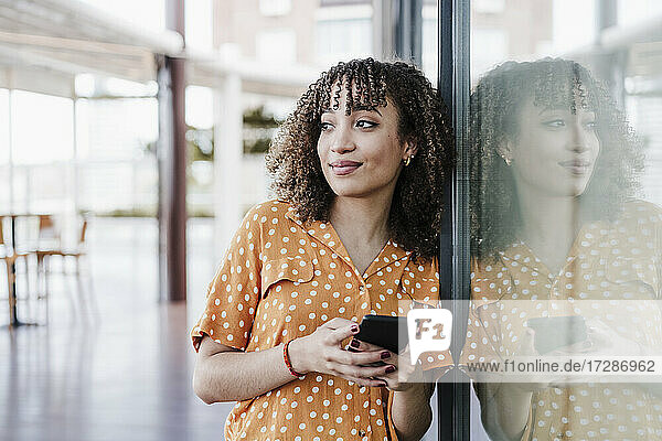 Beautiful young woman with mobile phone leaning on glass window