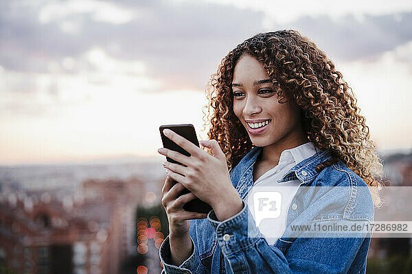 Lächelnde Frau mit Smartphone vor dem Himmel bei Sonnenuntergang