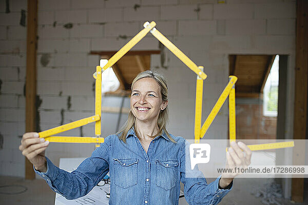 Glückliche Architektin  die auf der Baustelle mit einem Zollstock ein Haus formt