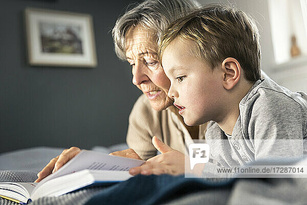 Großmutter liest ein Buch und liegt neben ihrem Enkel im Schlafzimmer
