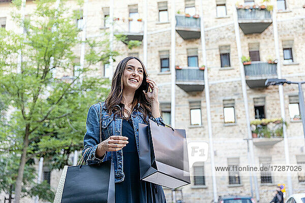 Lächelnde Frau mit Einkaufstüten  die in der Stadt mit einem Mobiltelefon spricht