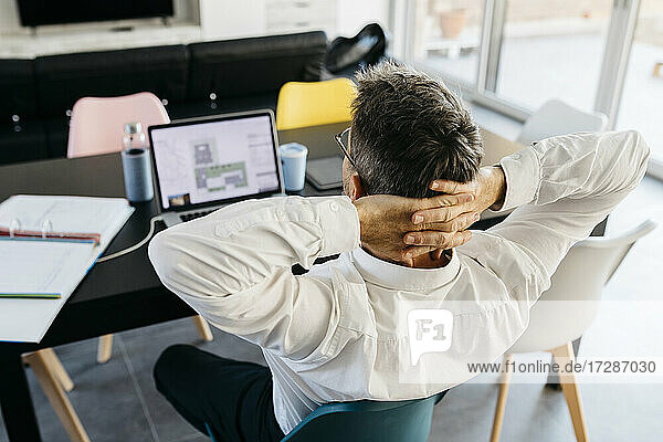Entspannte männliche Design-Profi mit Händen hinter dem Kopf sitzen vor dem Laptop im Büro zu Hause
