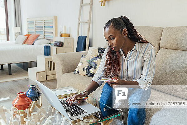Mittlere erwachsene Frau  die einen Laptop benutzt  während sie mit einem Notizblock zu Hause sitzt