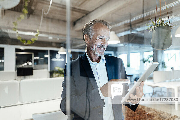 Smiling businessman using digital tablet behind glass wall