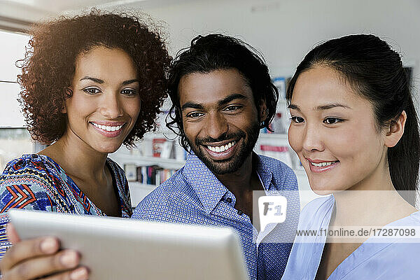 Smiling businessman with female colleagues looking at tablet while discussing in office