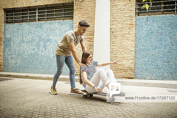Cheerful couple playing with skateboard on footpath