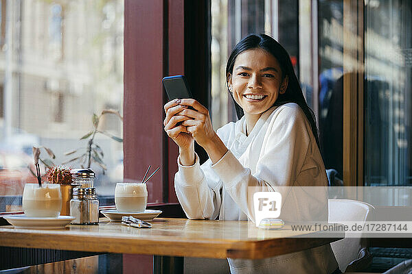 Glückliche Frau sitzt mit Smartphone in einem Café