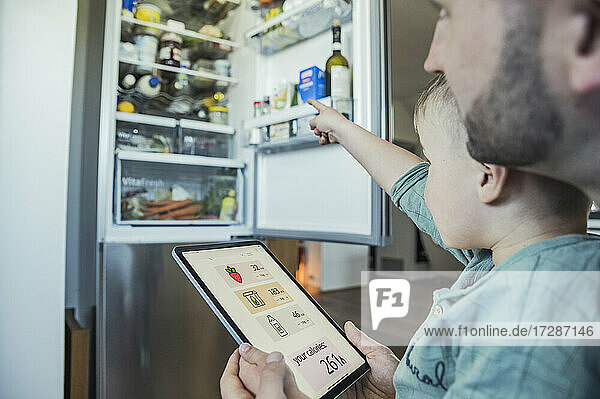 Junge mit Vater  der ein Tablet hält und auf den Kühlschrank in der Küche zeigt