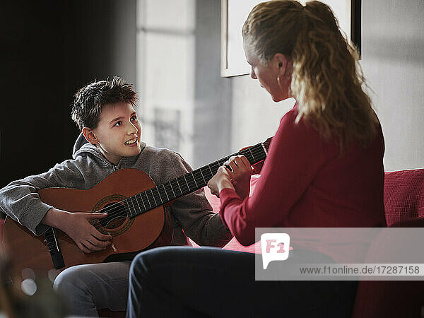 Mutter hilft ihrem Sohn beim Gitarre spielen zu Hause
