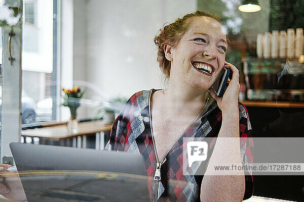 Happy mid adult woman looking away while talking on mobile phone in coffee shop