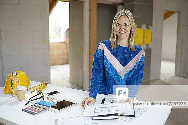 Lächelnde Architektin mit Bauplan am Tisch in einer Loftwohnung