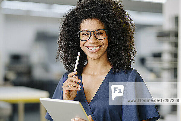 Smiling female entrepreneur holding digital tablet and digitized pen standing in office