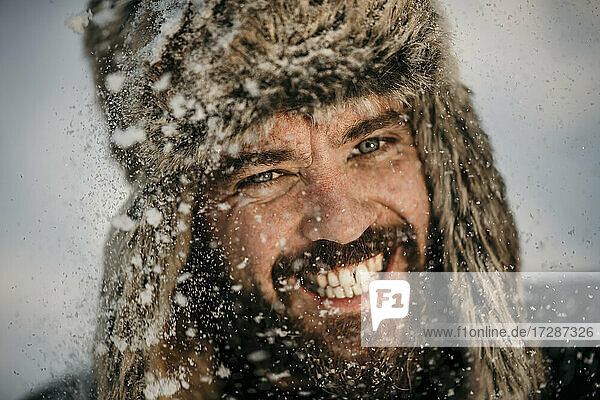Mid adult man wearing hunters cap smiling while snowing