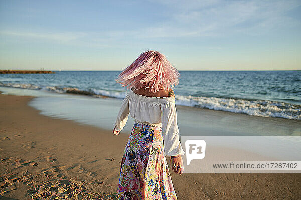 Frau mit zerzaustem Haar  die sich bei Sonnenuntergang am Strand dreht