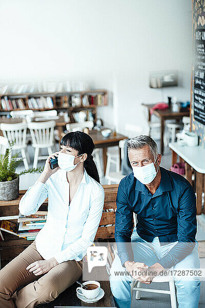 Männliche und weibliche Besitzer mit Gesichtsschutzmaske sitzen in einem Café