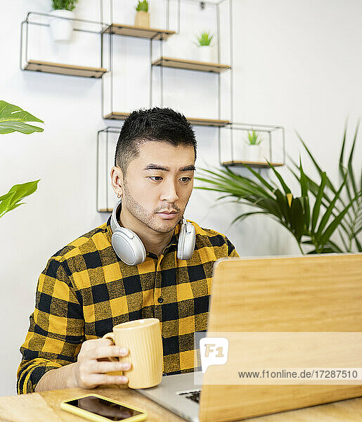 Junger Mann mit drahtlosen Kopfhörern und Laptop bei der Arbeit im Büro
