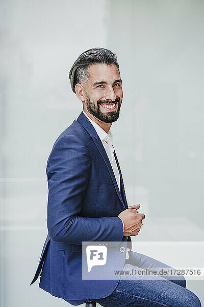 Businessman smiling while sitting by white wall