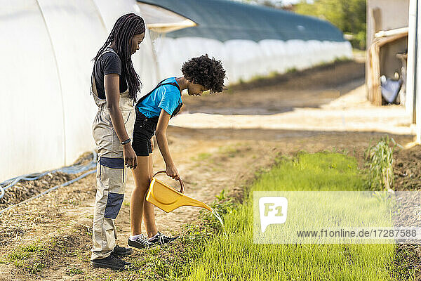 Bäuerin betrachtet Mädchen beim Gießen von Pflanzen auf einem Biohof