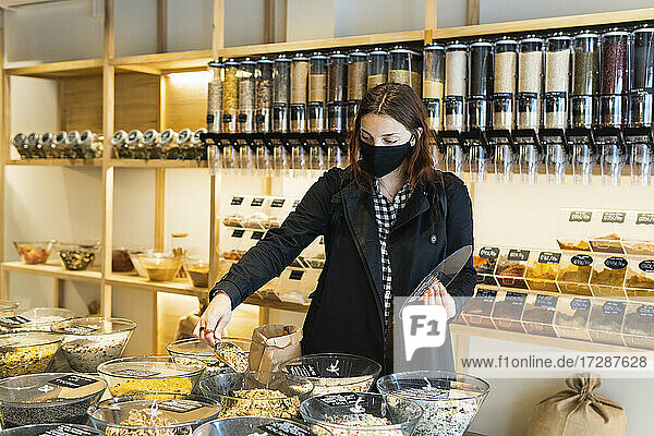 Young woman filling ingredients in paper bag during COVID-19 at store