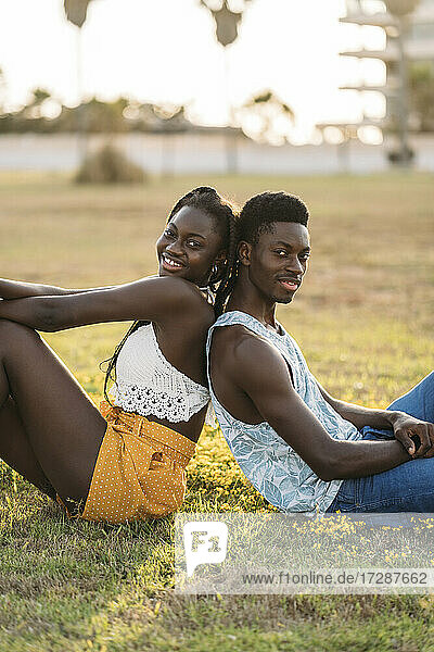 Smiling couple leaning while sitting back to back at grass area