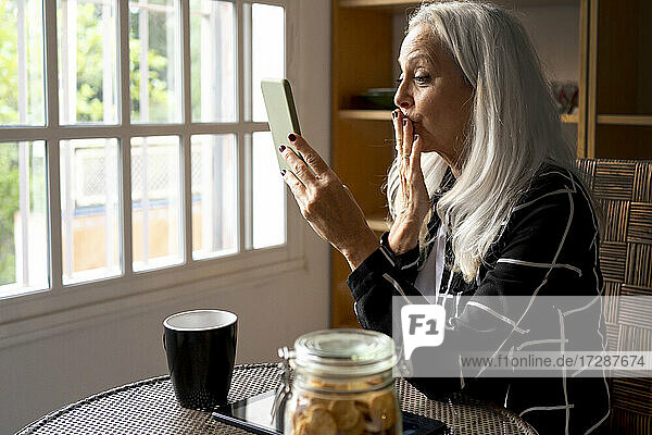Senior woman blowing kiss during video call through smart phone at home