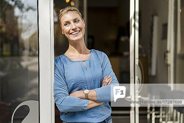 Happy businesswoman standing with arms crossed at doorway looking away