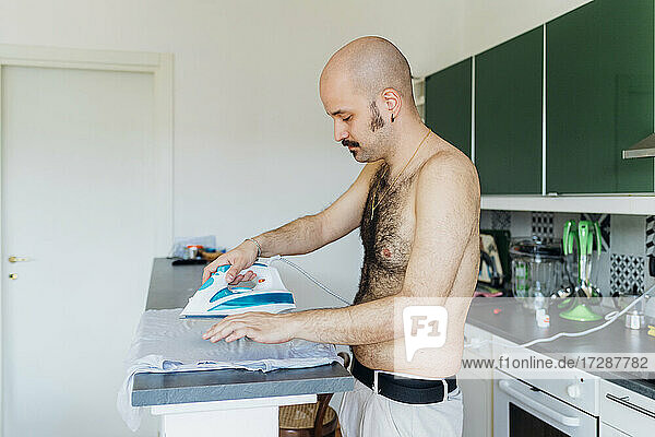 Hemdenloser Mann bügelt Hemd auf Kücheninsel zu Hause