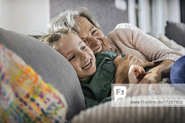 Happy grandmother and granddaughter resting on sofa in living room