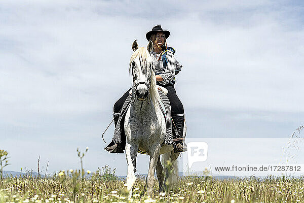 Junge Frau auf einem Pferd sitzend und wegschauend an einem sonnigen Tag