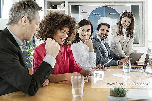 Lächelnde männliche und weibliche Fachkräfte  die ihre Kollegen bei der Diskussion über ein Grafiktablett im Büro beobachten