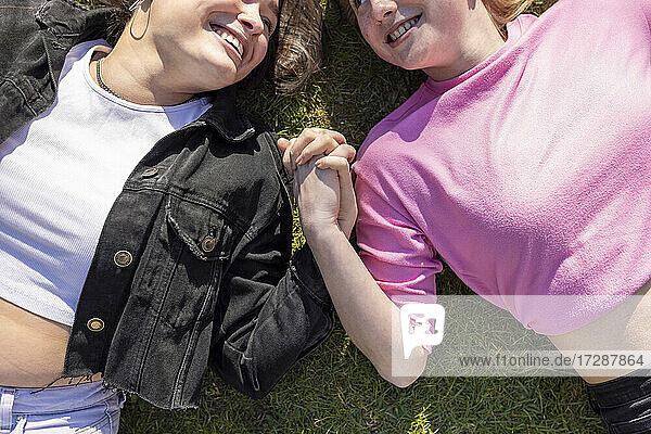 Glückliche Freundinnen  die sich an den Händen halten und auf dem Gras in einem öffentlichen Park liegen