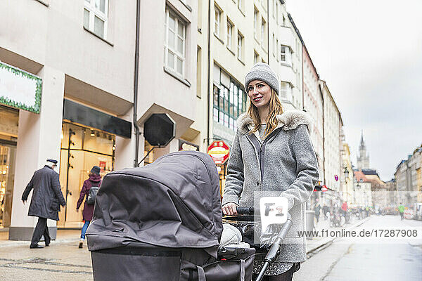 Mother pushing baby stroller while walking on street in city