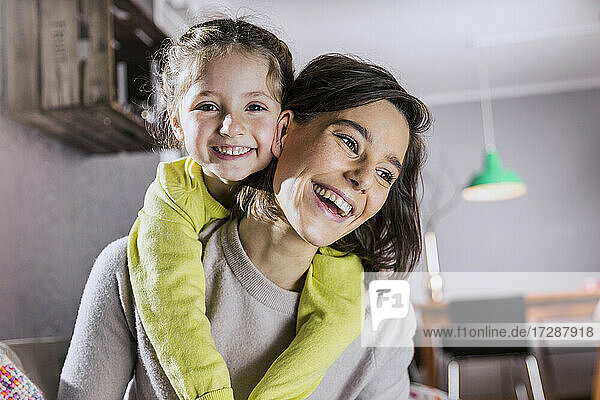 Smiling mother piggybacking daughter at home