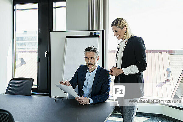 Weibliche Fachkraft  die einen Geschäftsmann ansieht  der über ein Dokument diskutiert  während er im Sitzungssaal etwas erklärt