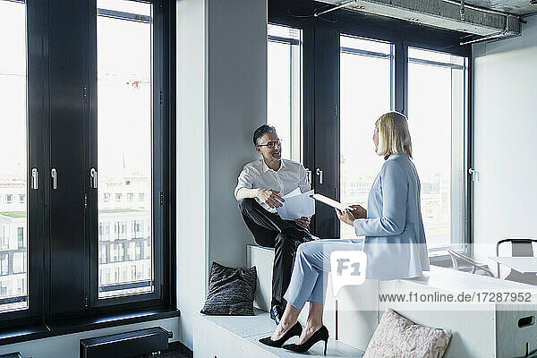 Männliche und weibliche Unternehmer diskutieren zusammen  während sie auf Möbeln im Büro sitzen