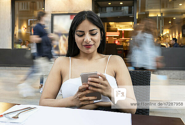 Junge Frau benutzt ihr Smartphone  während sie in einem Café am Tisch sitzt